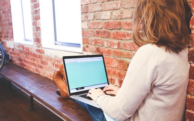 a person sitting with a computer on the lap and typing in a notebook